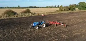 Image of a tractor being self-driven by an automated system with land tiller behind, tilling a field on the Hands Free Farm